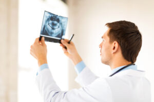 A man in a lab coat examines a dental X-ray against a light background.